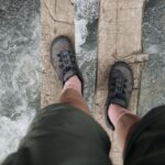 Hiker in grey trail shoes balancing on a wooden log above a flowing river