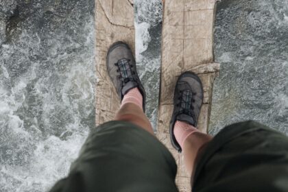 Hiker in grey trail shoes balancing on a wooden log above a flowing river