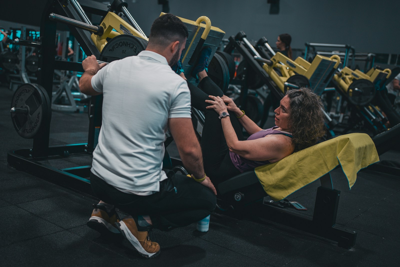 Illustrative photograph of a personal trainer coaching a woman through a strength workout in a gym