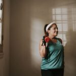 Middle-aged woman in workout clothes lifting a dumbbell indoors